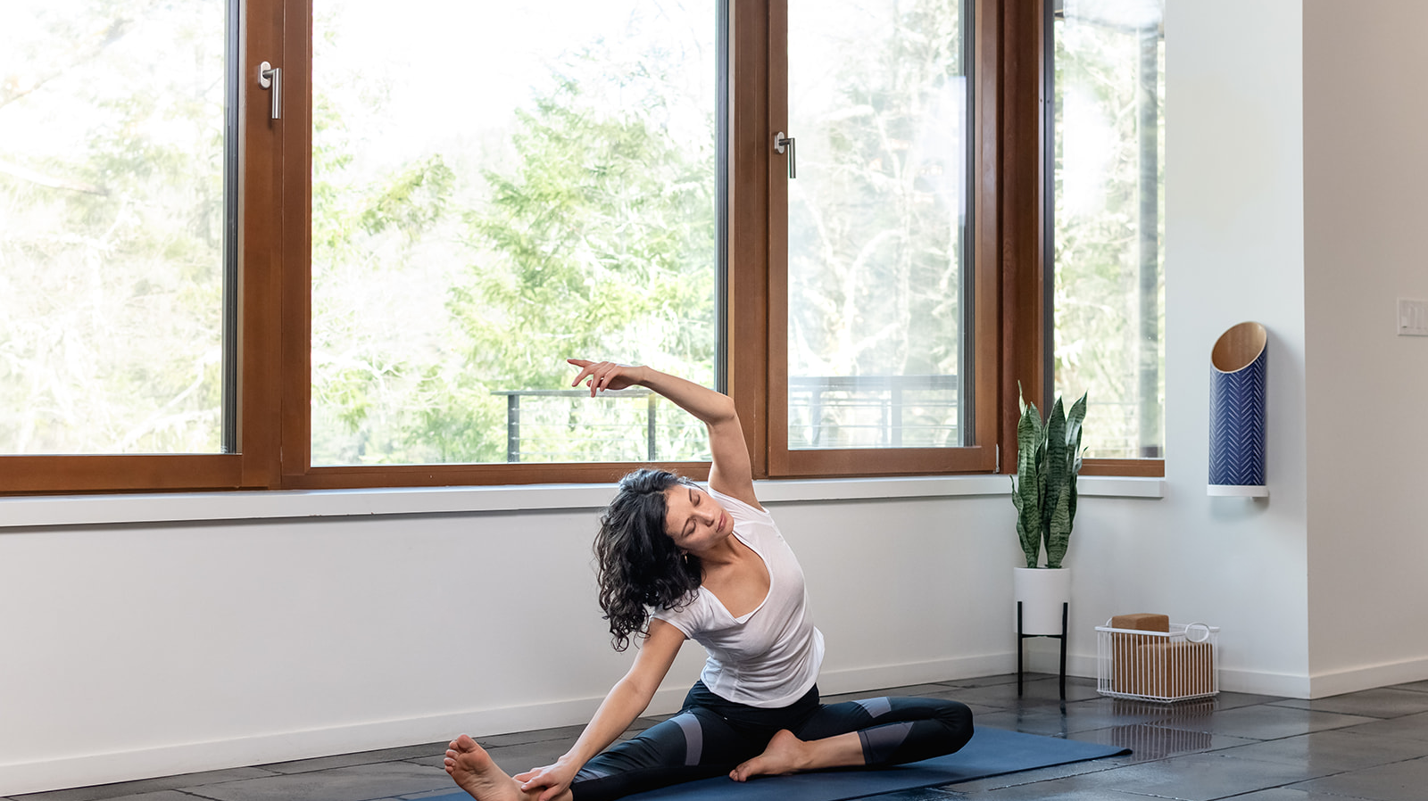 woman practicing yoga in front of a window in a home yoga studio with sustainable yoga prop storage