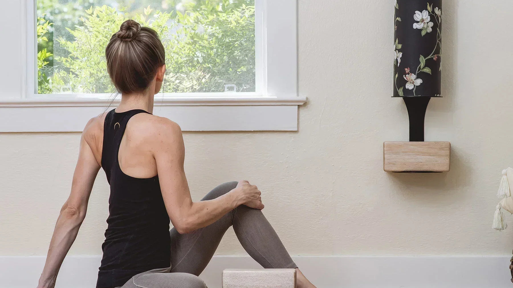 Woman practicing yoga on an eco-friendly yoga mat beside a yoga block and Mache Homi Wall Bracket storage.