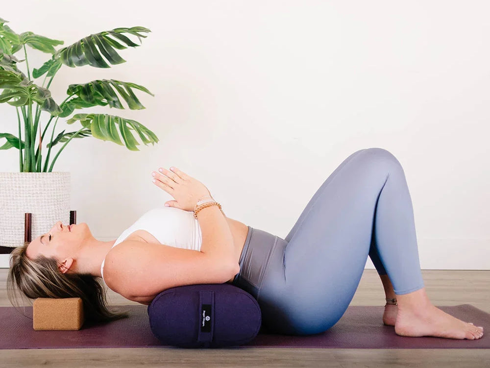 Woman using Mache eco-friendly cotton-covered yoga bolster to support her spine during a beginner-friendly reclined pose.