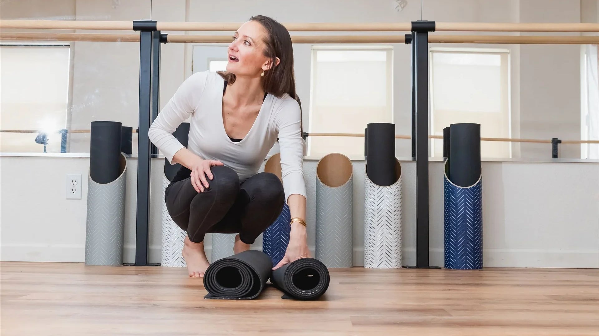 Woman organizing rolled Mache yoga mats in a yoga studio, highlighting thoughtful mat storage and care.