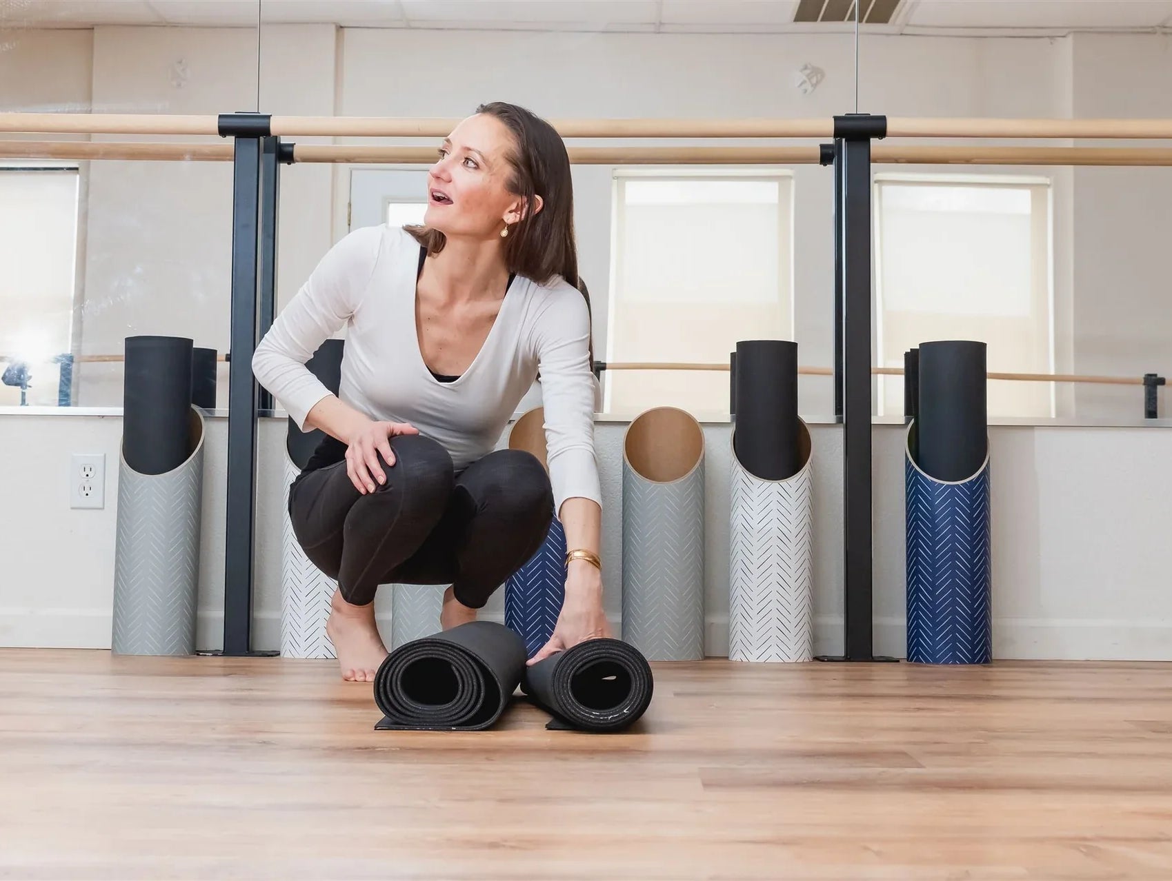 Woman organizing rolled Mache yoga mats in a yoga studio, highlighting thoughtful mat storage and care.