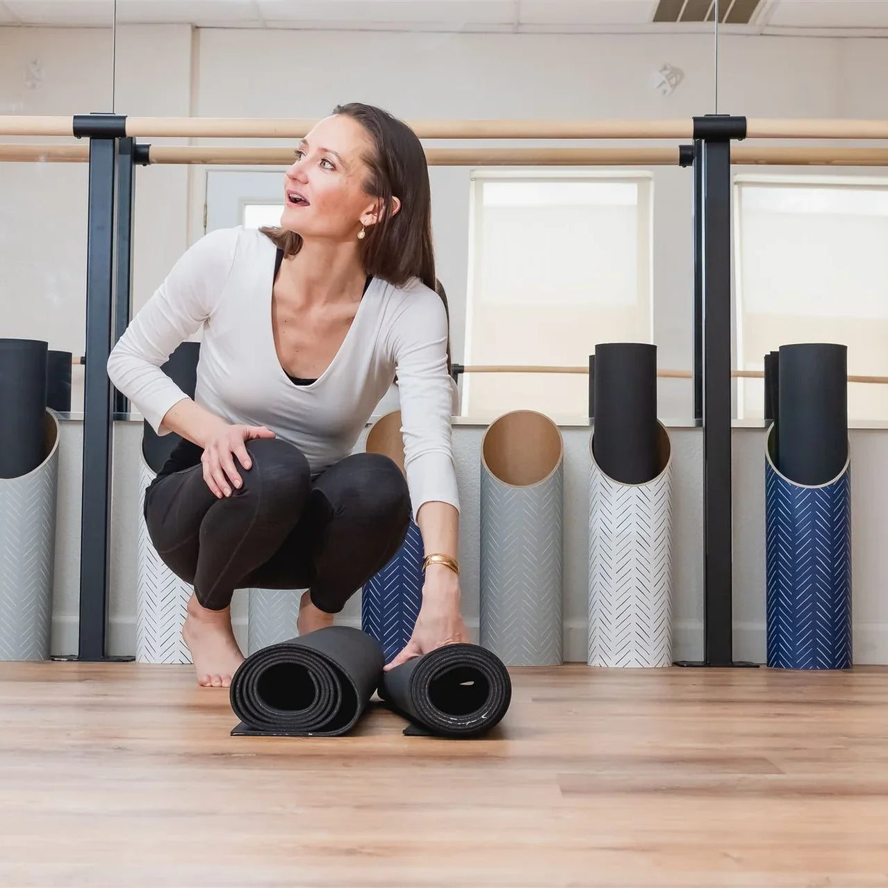 Woman organizing rolled Mache yoga mats in a yoga studio, highlighting thoughtful mat storage and care.