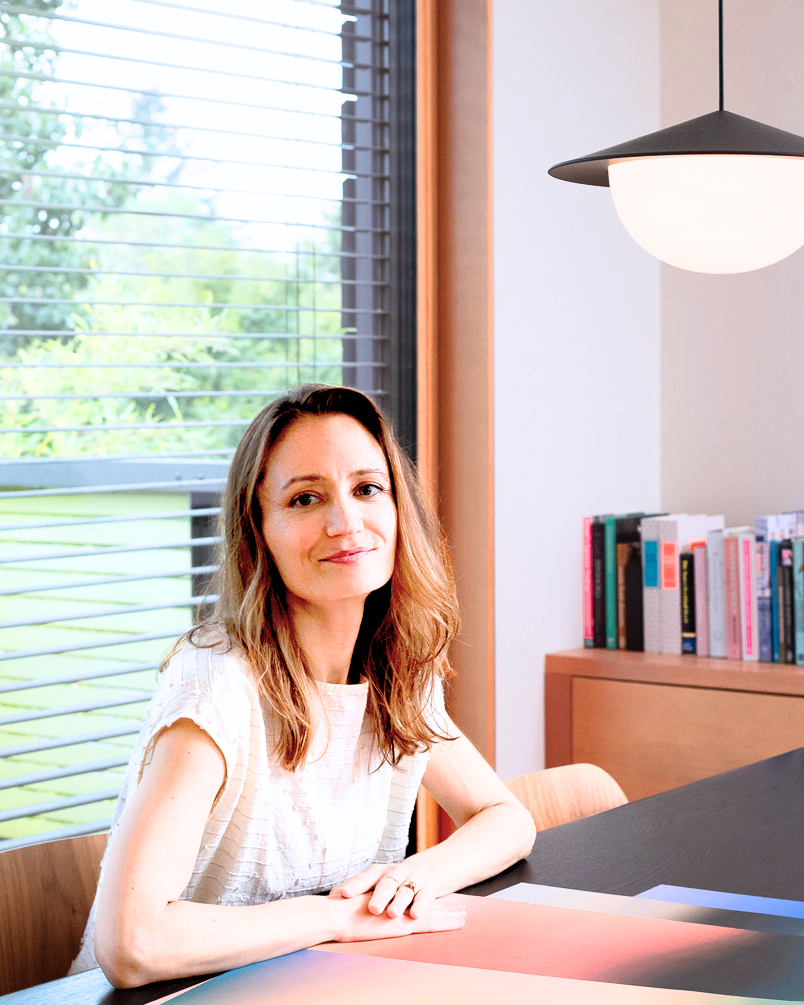 Wellness Designer Brienne sitting at a desk in a modern office setting with large windows.