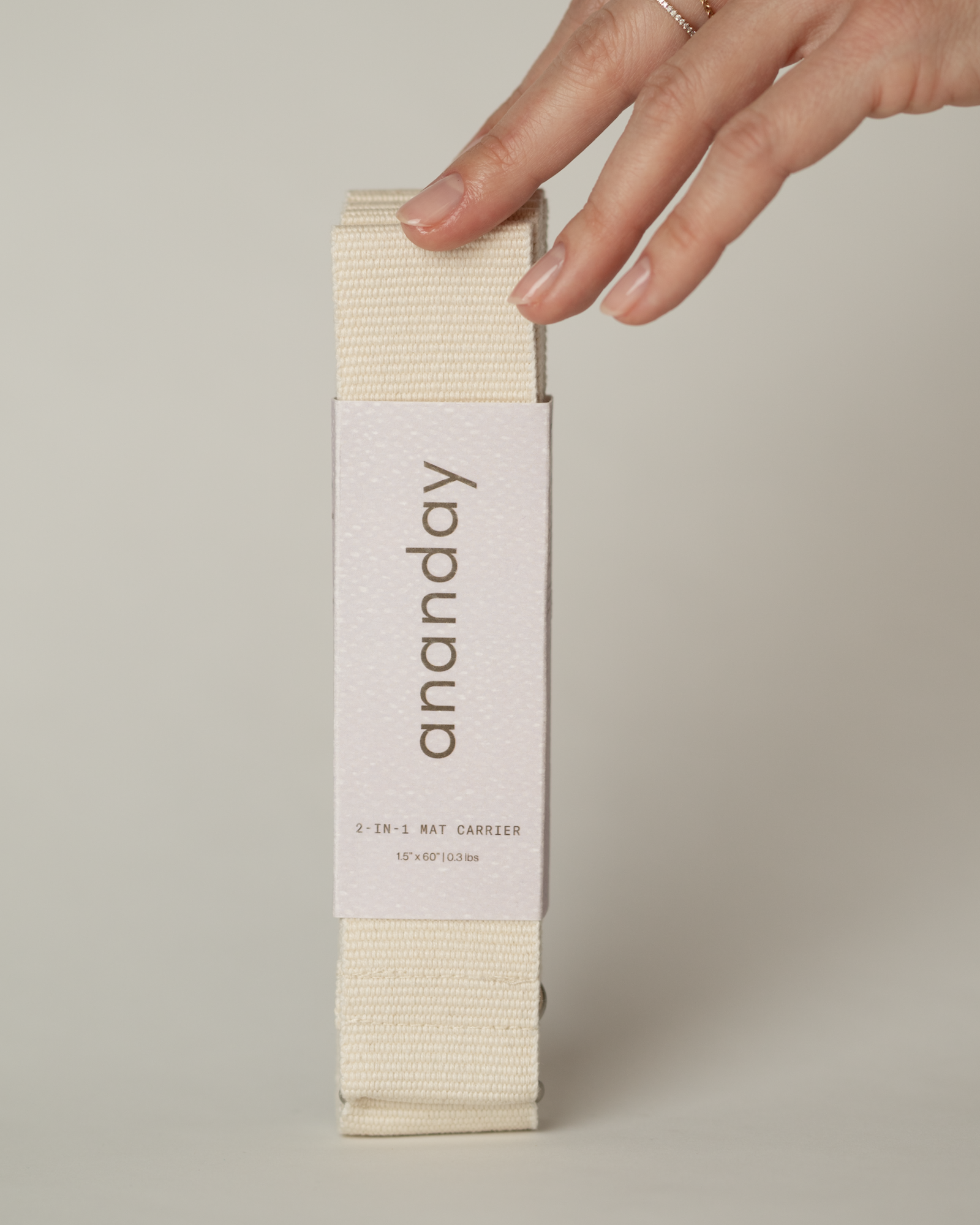 Hand holding a combination yoga strap/yoga sling in 'ananday' packaging on a neutral background