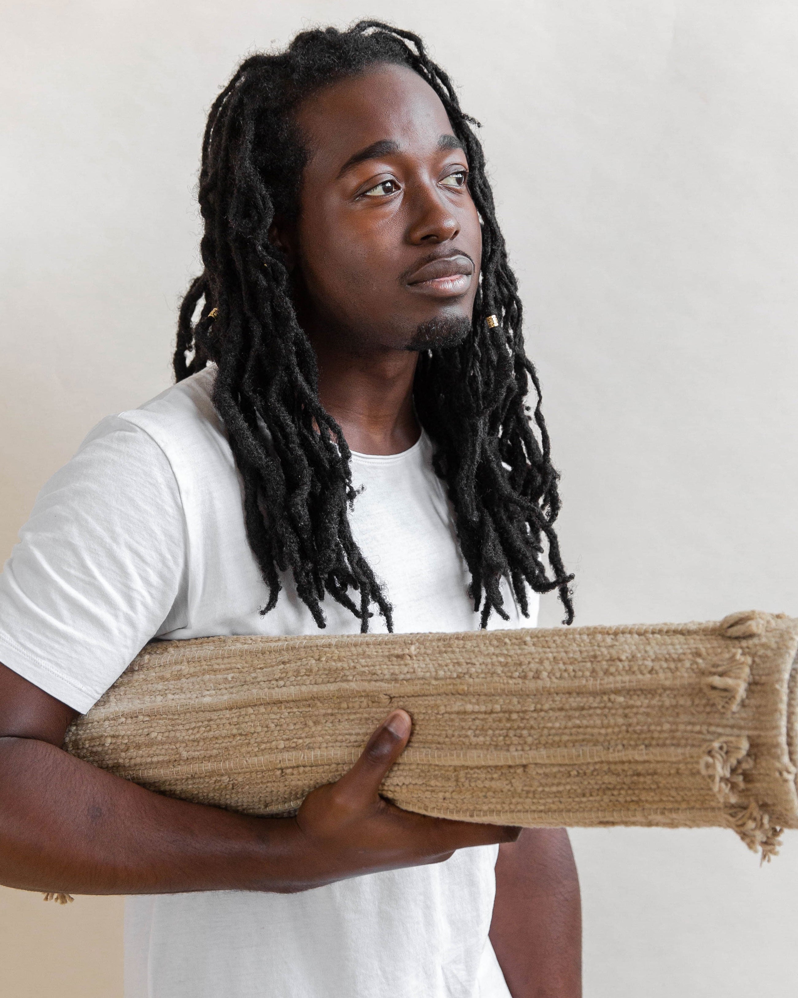 Man holding a rolled-up jute rug against a plain background