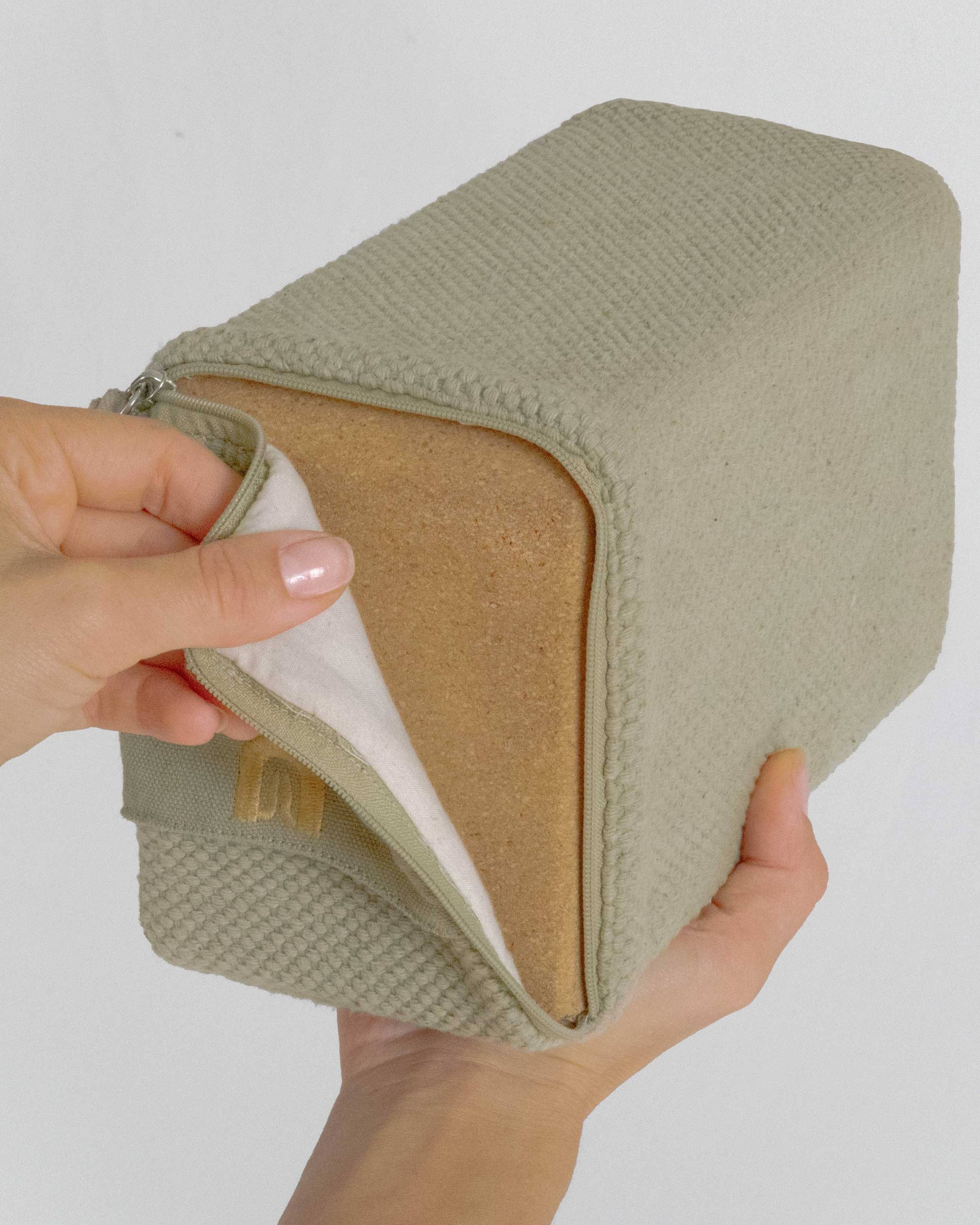 Hand holding a beige fabric block with a white interior against a plain background