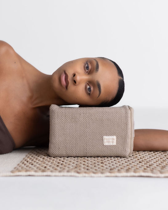 Woman lying on a mat with a beige yoga block on her arm against a white background
