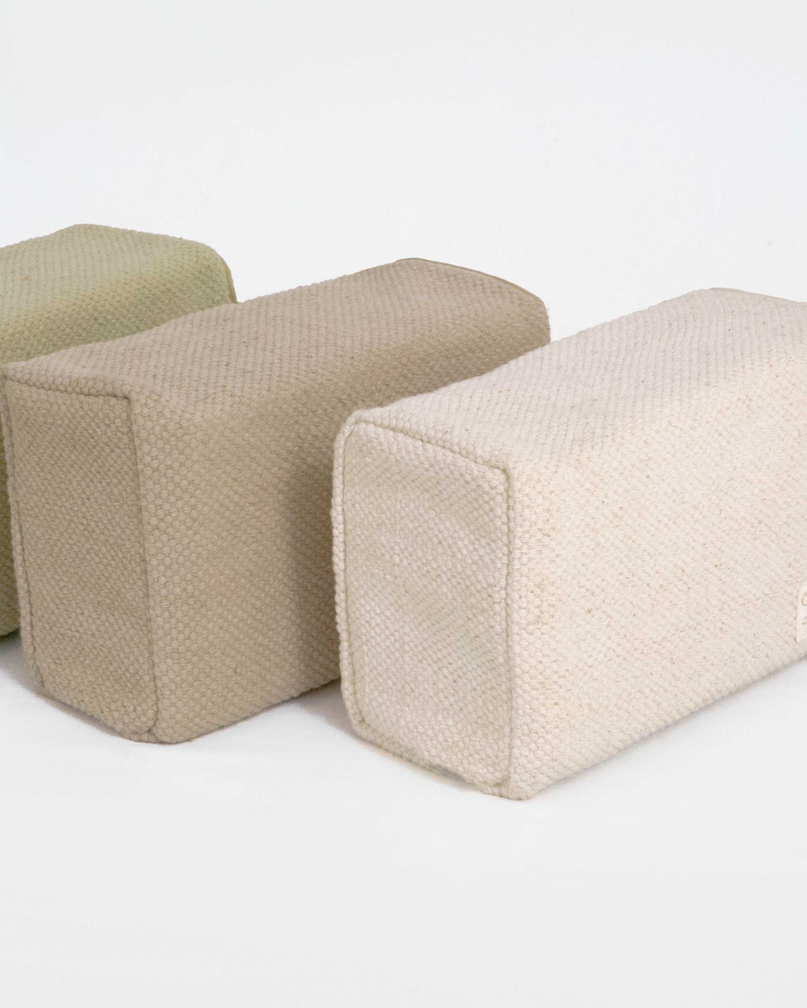 Three rectangular fabric yoga blocks in beige and brown on a white background