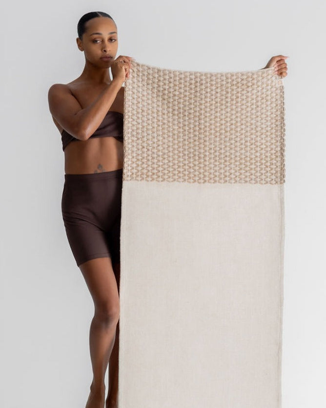 Woman holding a woven yoga rug with a white and beige pattern on a white background