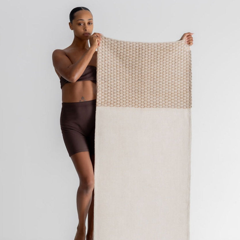 Woman holding a woven yoga rug with a white and beige pattern on a white background