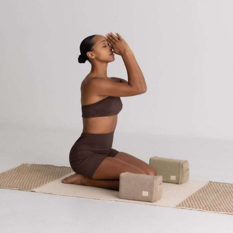 Woman in brown athletic wear practicing yoga on a mat with yoga blocks against a plain background