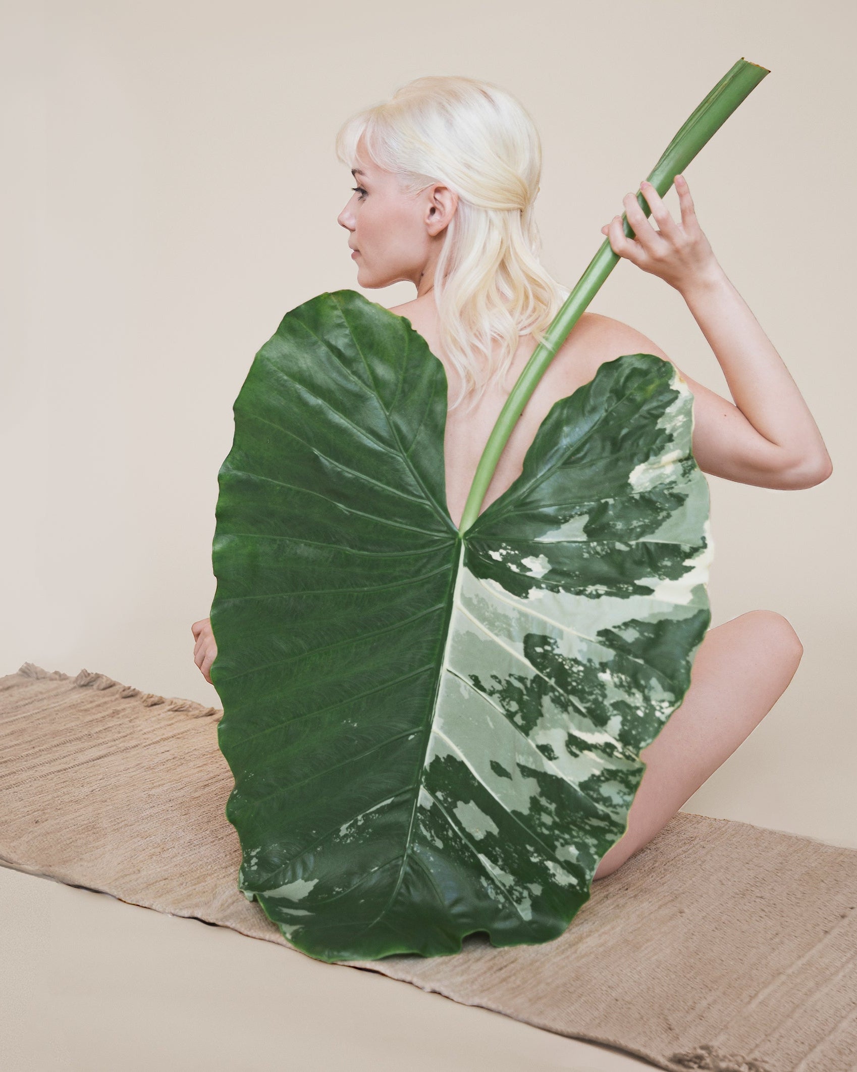 Person holding a large green leaf against a plain background, on a luxury textile yoga mat