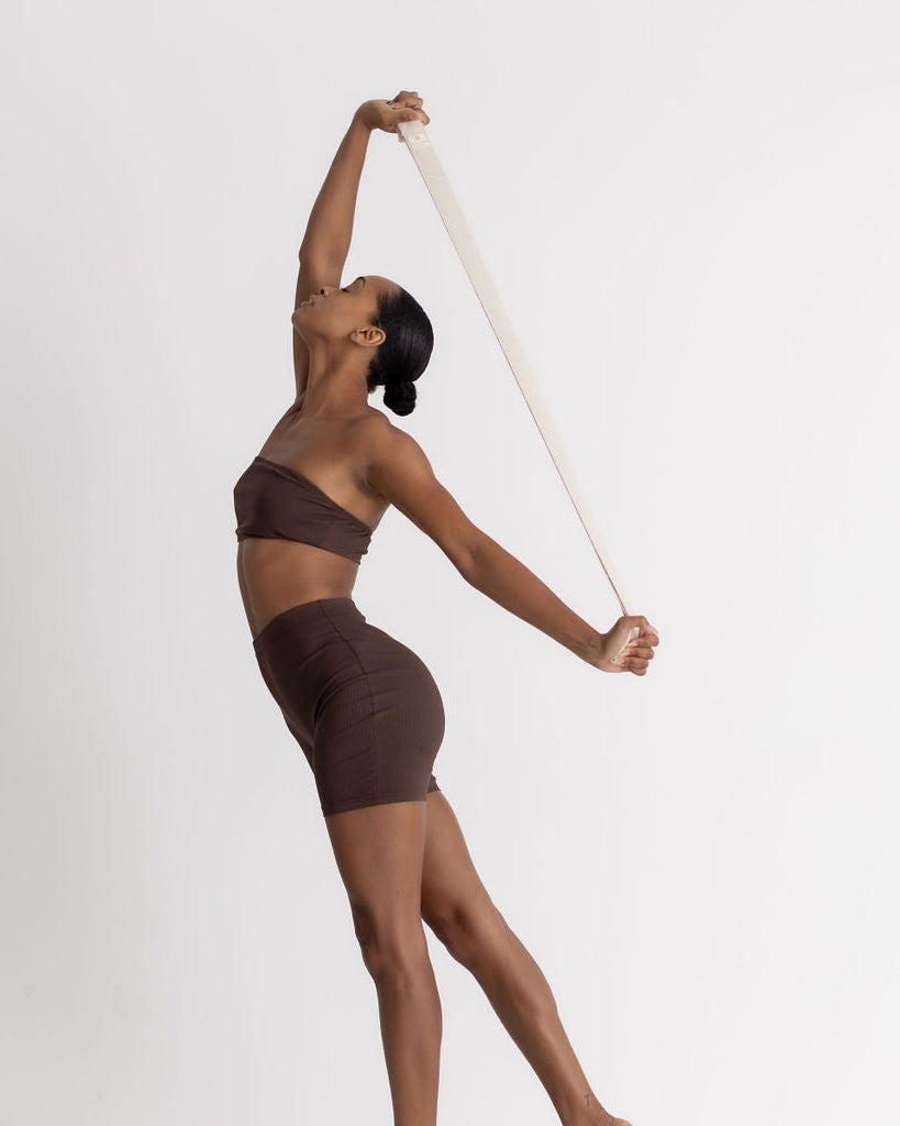 Dancer in a brown outfit holding a cream yoga strap against a white background