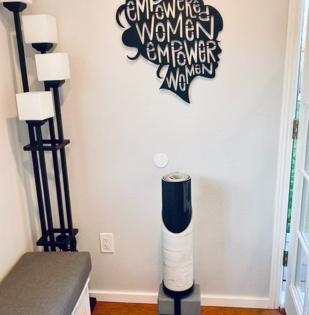 Yoga Mat Holder with Floor Stand in Front of Grey Wall with "Empowered Women Empower Women" Motif