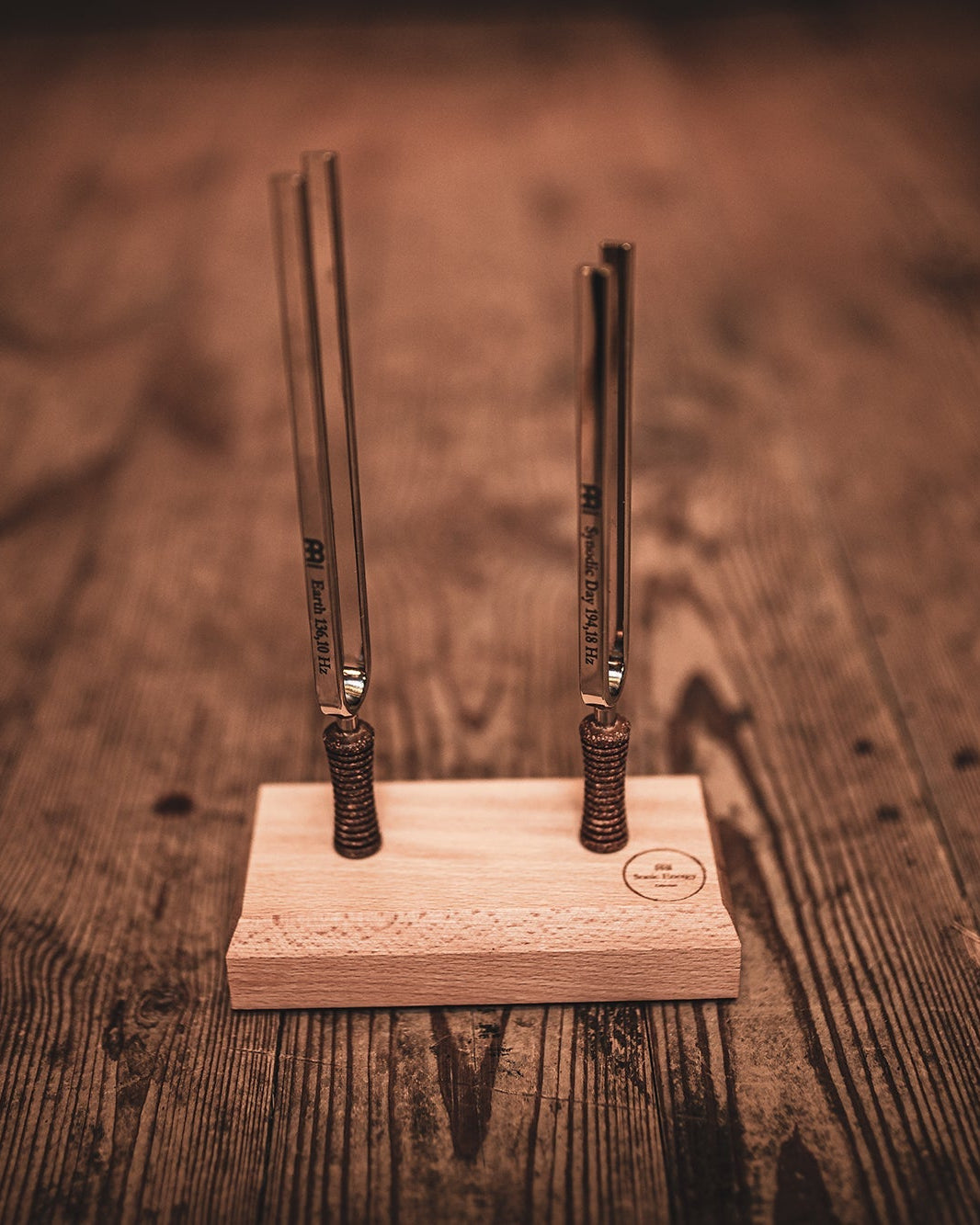 Two metal tuning forks on a wooden stand against a wooden background