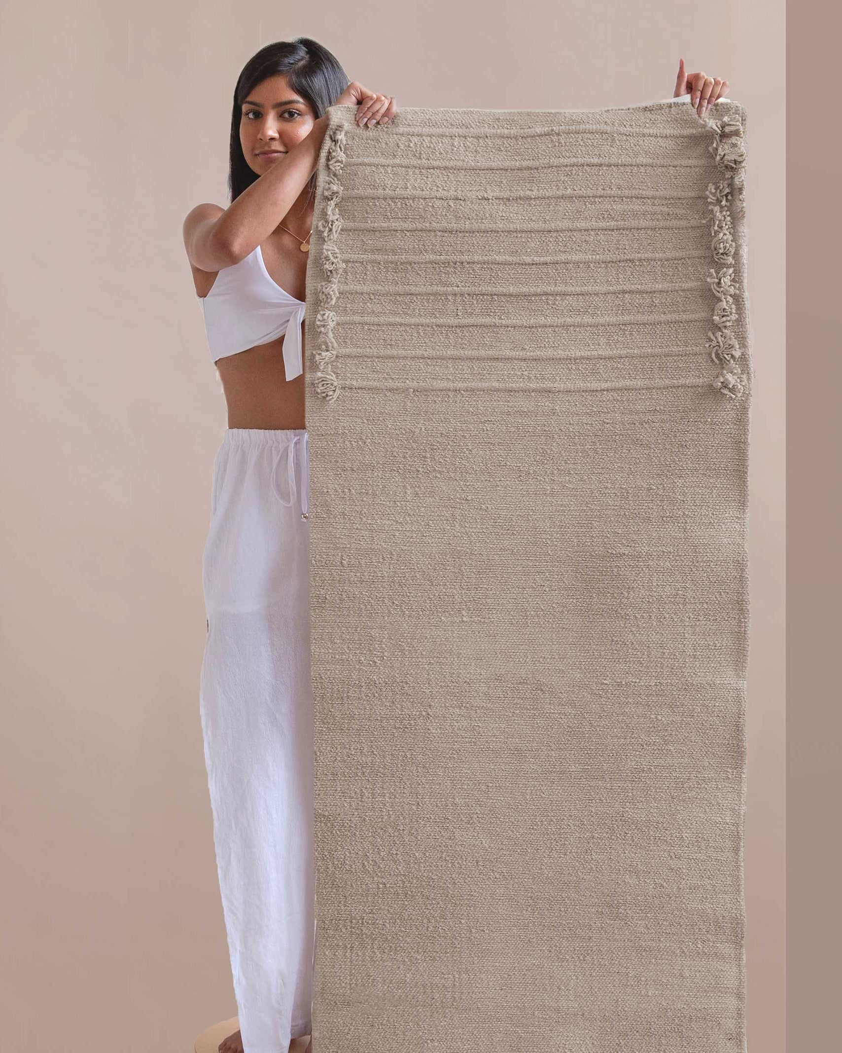 Woman holding a textured fabric yoga mat against a beige background