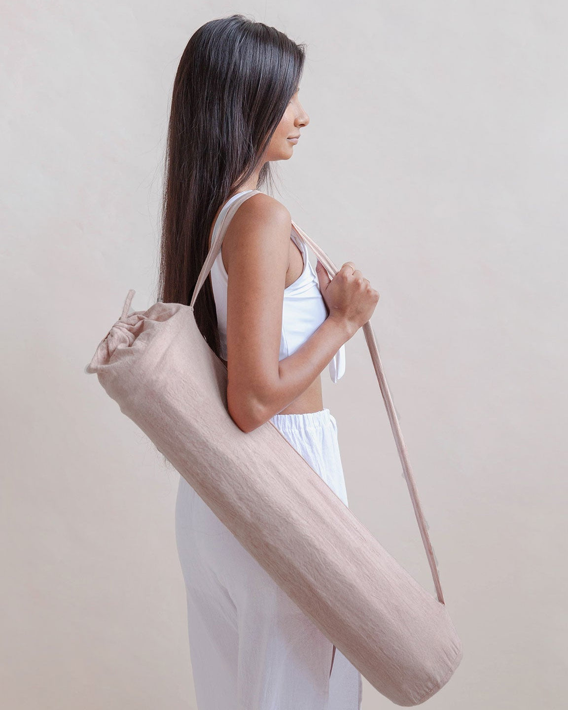 Woman holding a beige yoga mat bag against a plain background