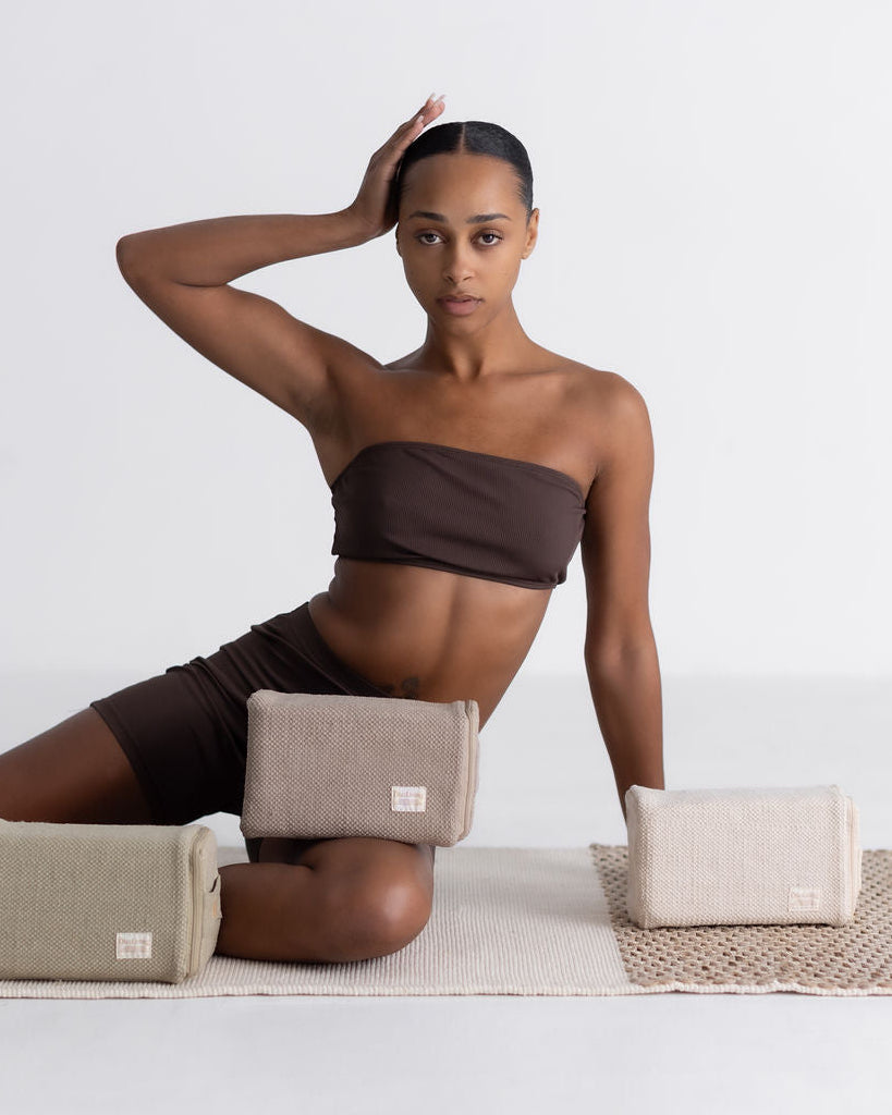 Woman sitting on a mat with cotton yoga blocks around her, against a plain background