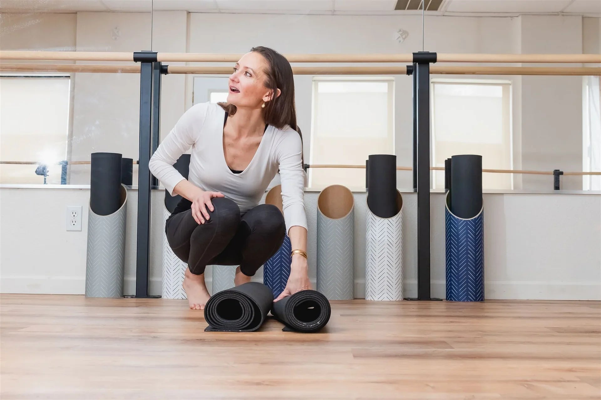 Woman organizing rolled Mache yoga mats in a yoga studio, highlighting thoughtful mat storage and care.