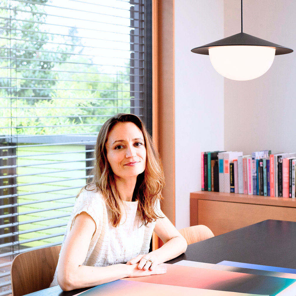 Wellness Designer Brienne sitting at a desk in a modern office setting with large windows.
