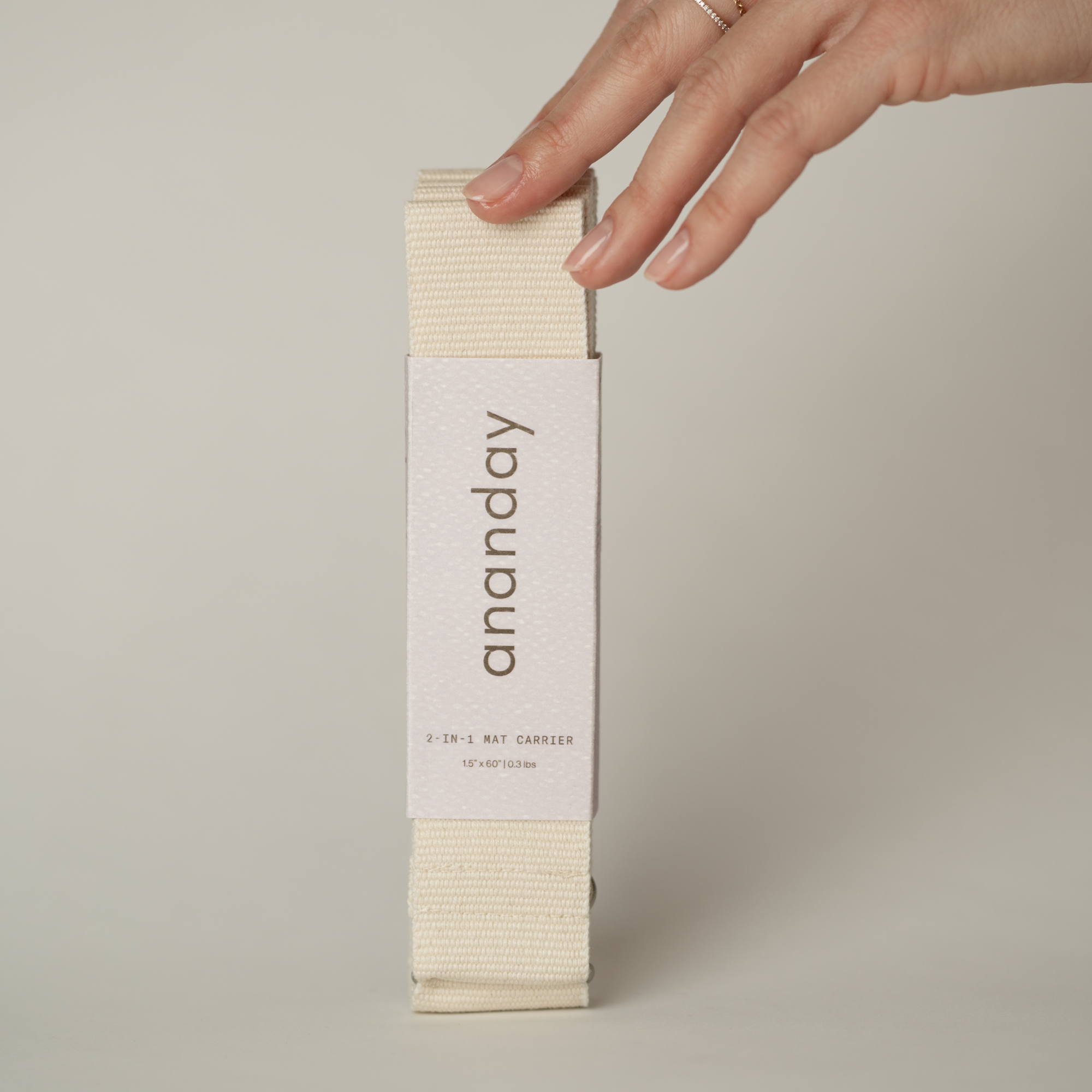 Hand holding a combination yoga strap/yoga sling in 'ananday' packaging on a neutral background