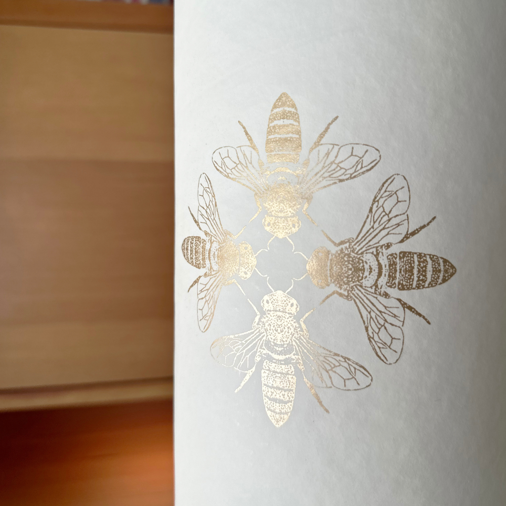 A yoga mat tube in a neutral color with a gold pattern, standing on top of a gold-colored yoga block floor stand.