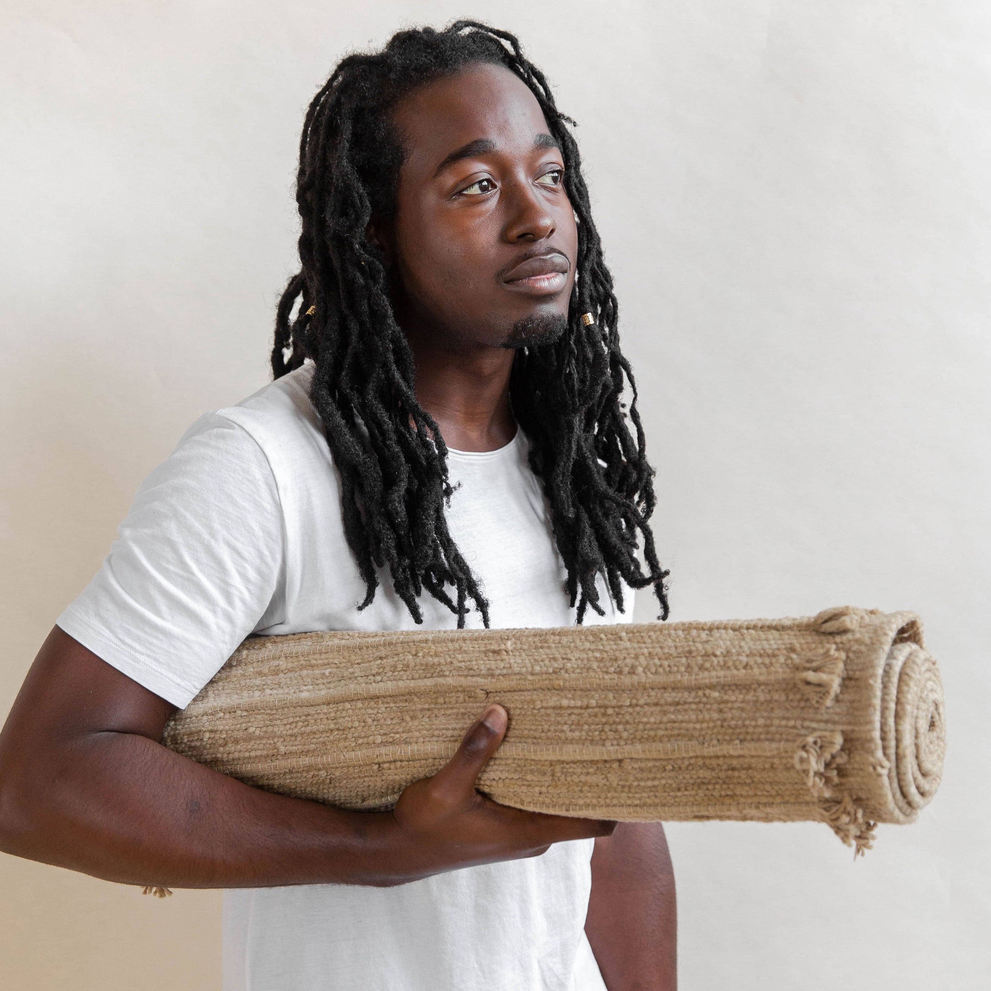 Man holding a rolled-up jute rug against a plain background