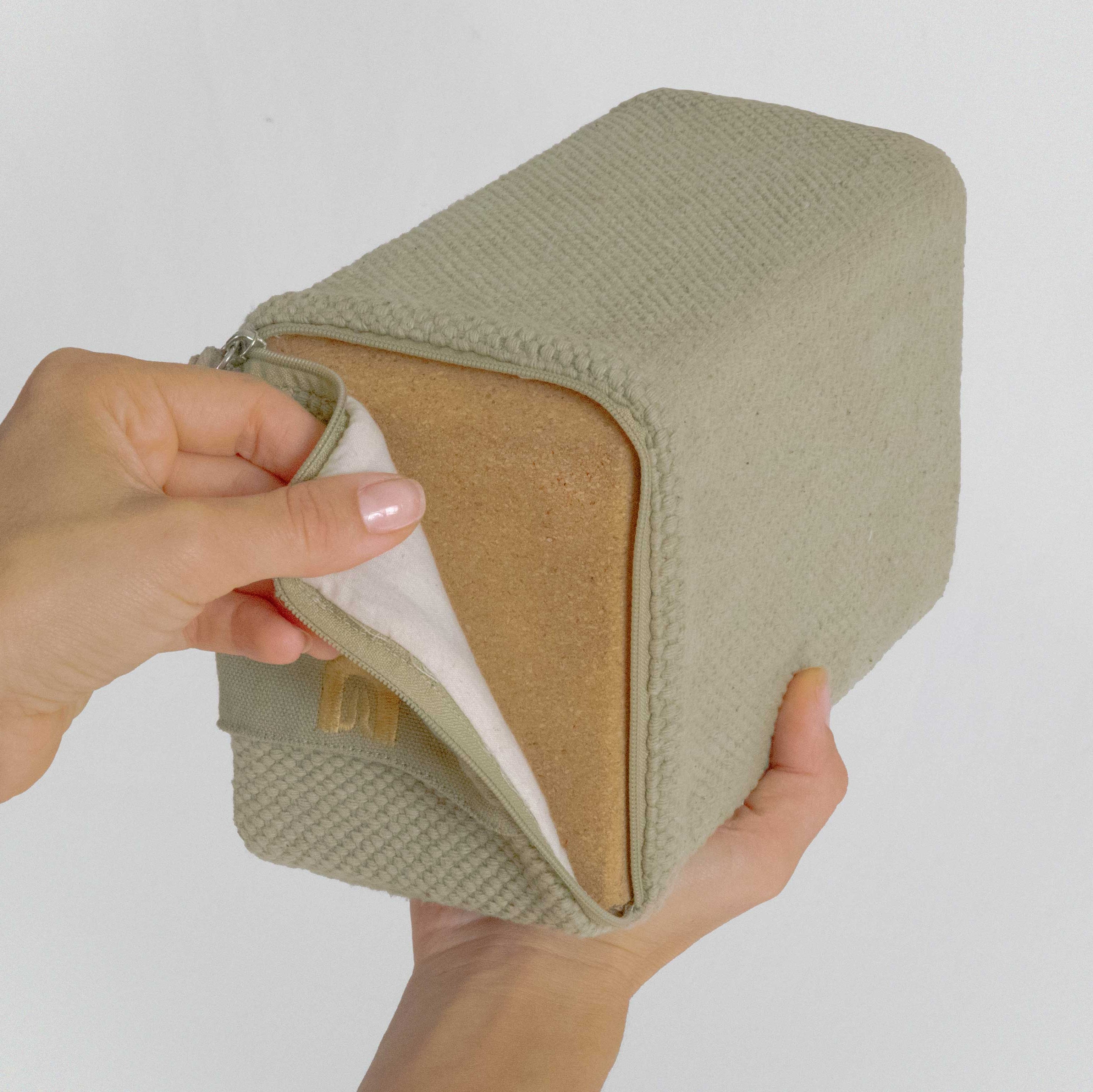 Hand holding a beige fabric block with a white interior against a plain background