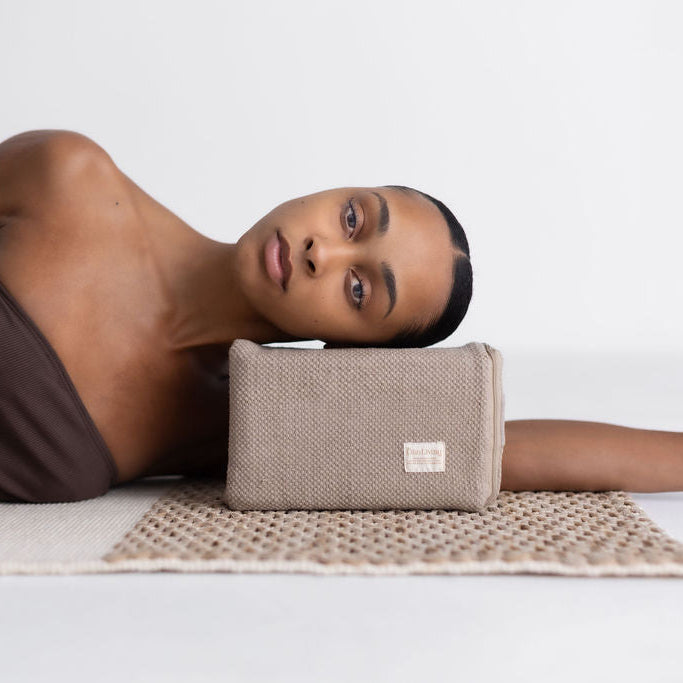 Woman lying on a mat with a beige yoga block on her arm against a white background