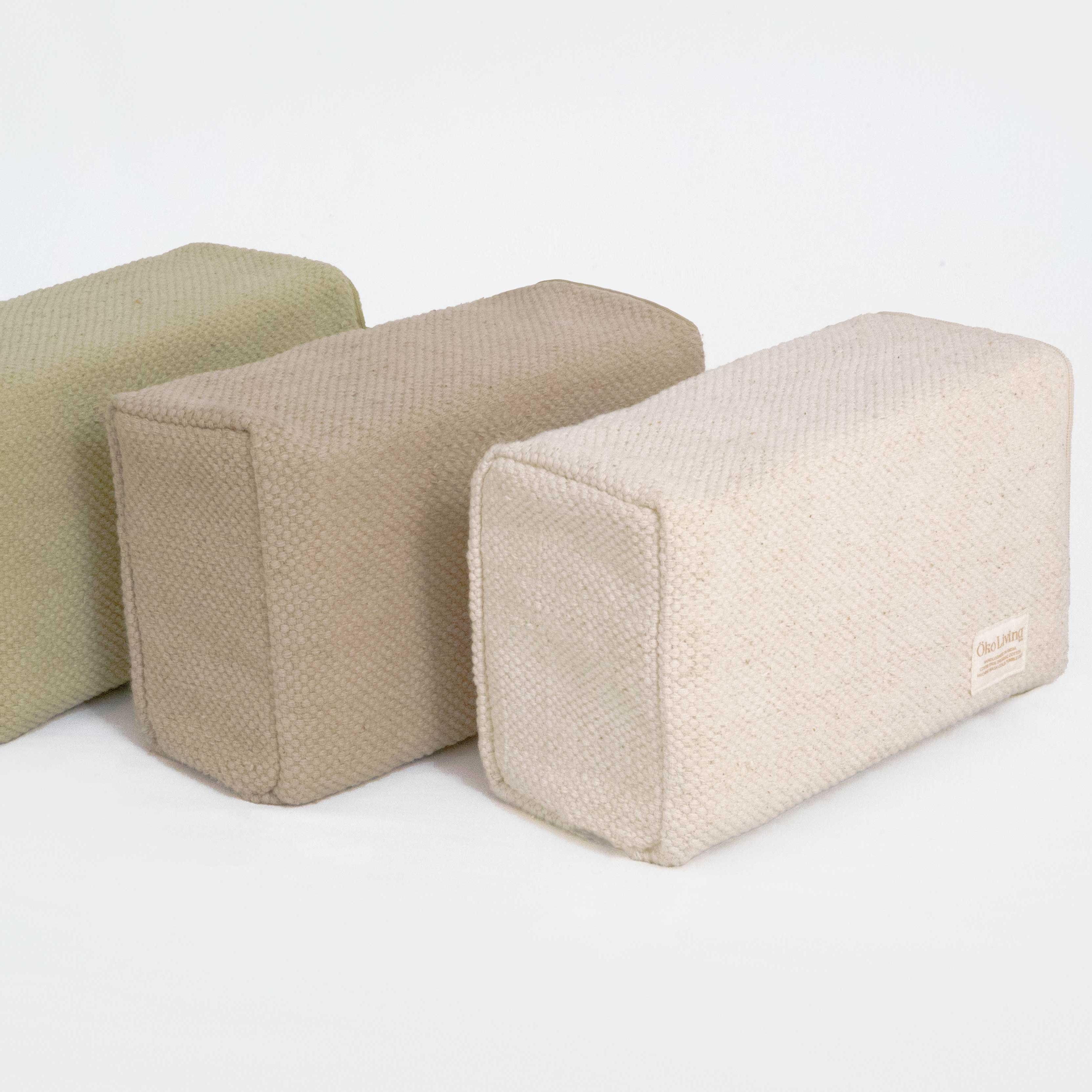 Three rectangular fabric yoga blocks in beige and brown on a white background