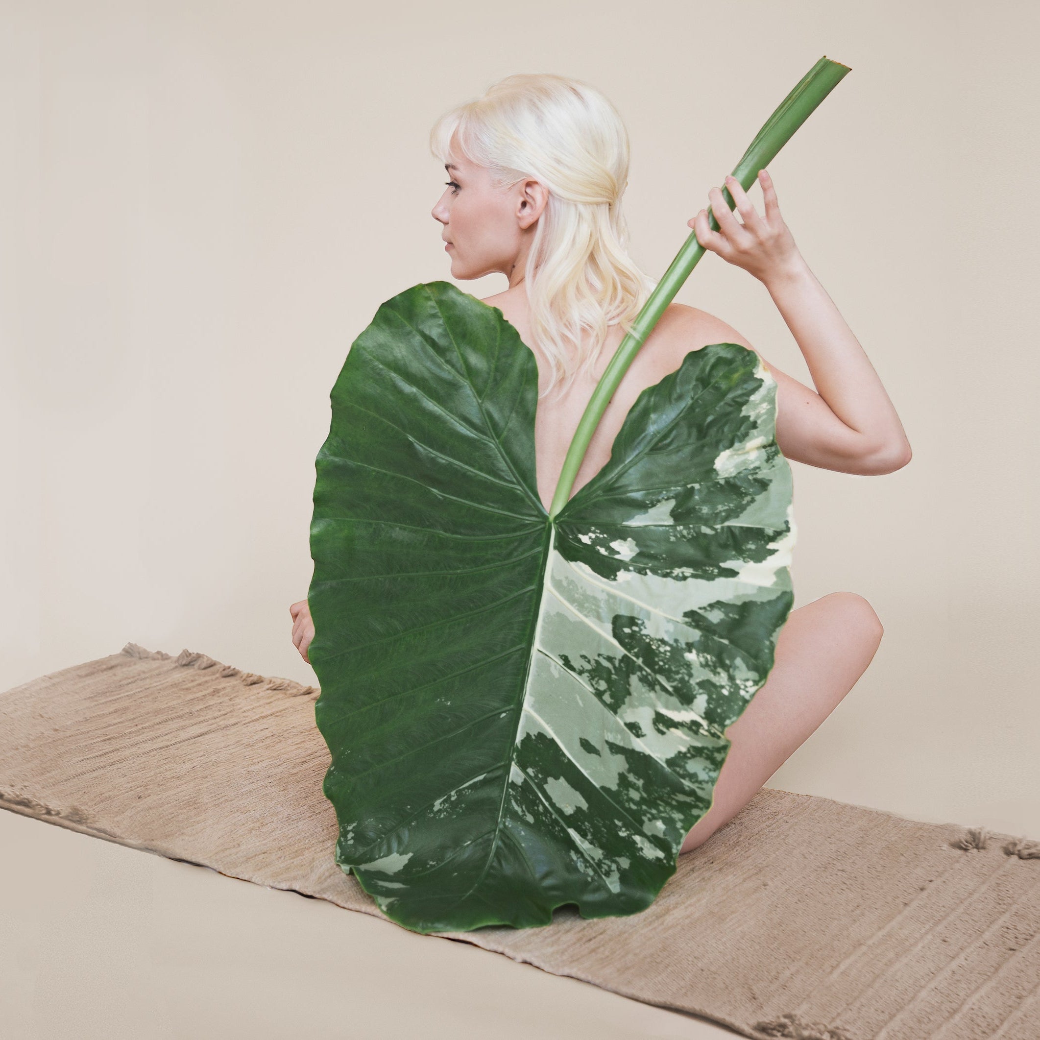 Person holding a large green leaf against a plain background, on a luxury textile yoga mat