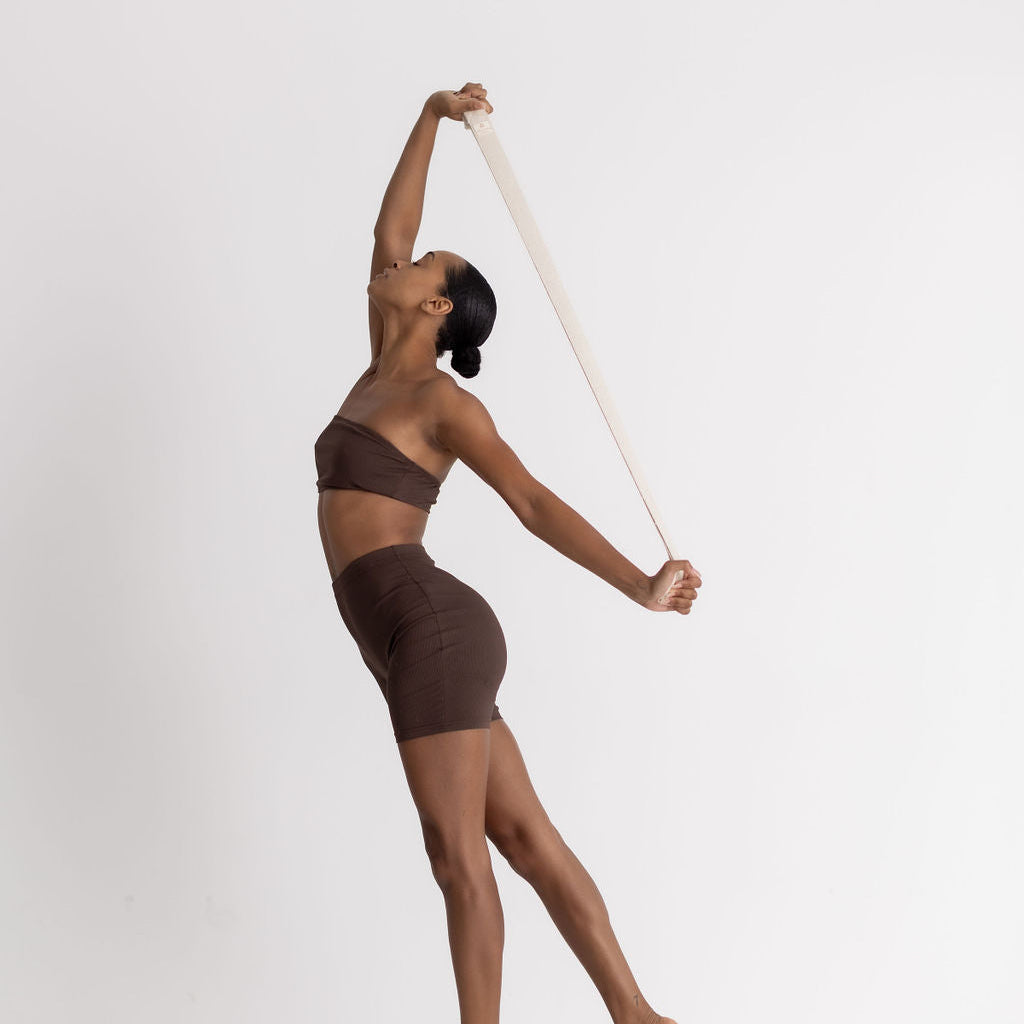 Dancer in a brown outfit holding a cream yoga strap against a white background