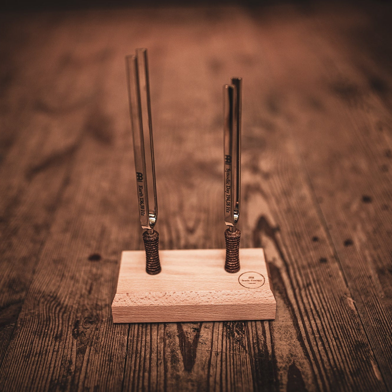 Two metal tuning forks on a wooden stand against a wooden background