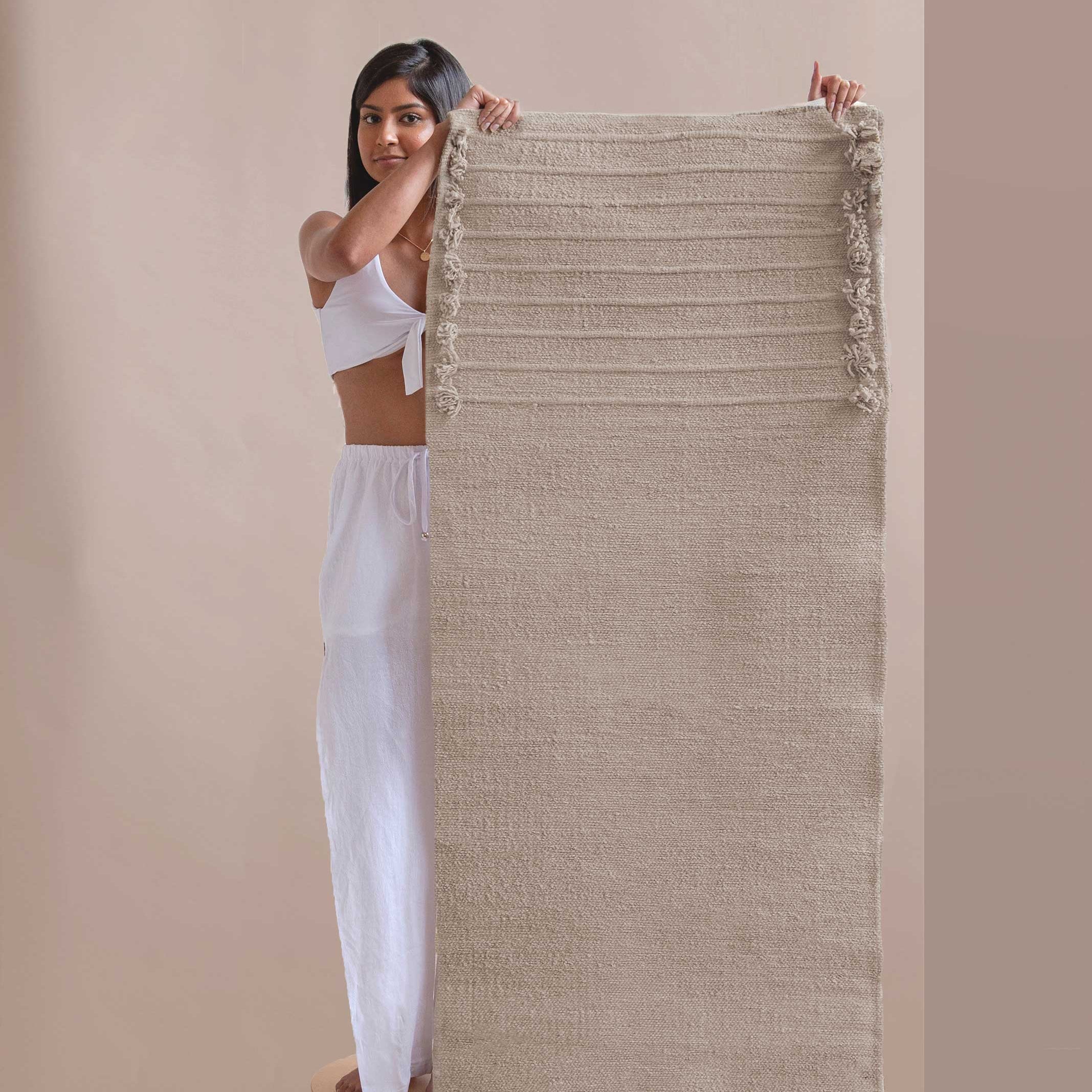 Woman holding a textured fabric yoga mat against a beige background