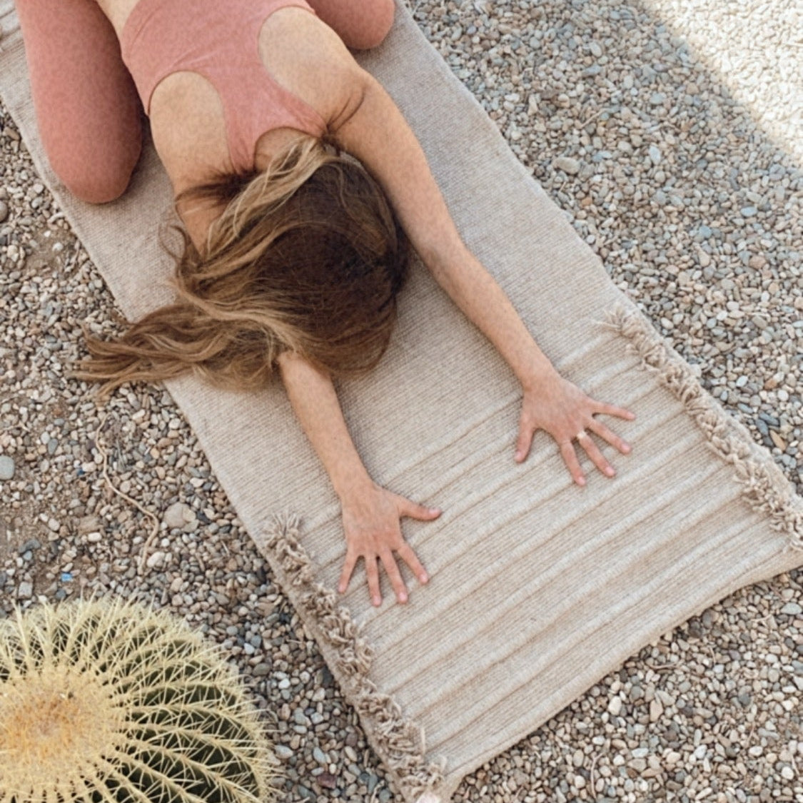 Person lying on a cotton woven yoga mat outdoors with a cactus plant nearby