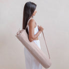 Woman holding a beige yoga mat bag against a plain background