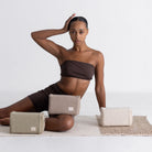 Woman sitting on a mat with cotton yoga blocks around her, against a plain background